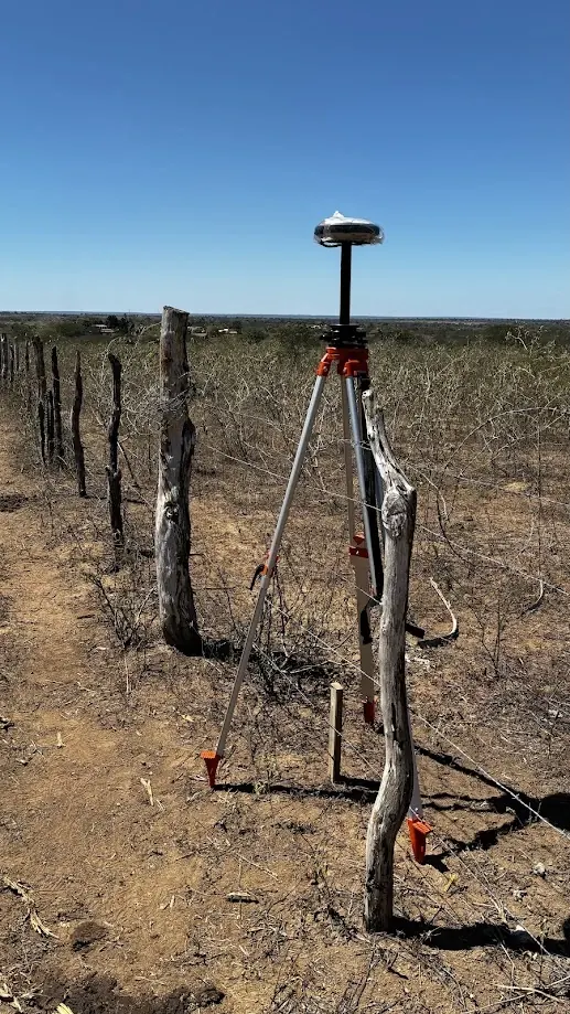 Receptor GNSS em tripé ao lado de uma cerca de estacas, em área de Caatinga sob céu limpo
