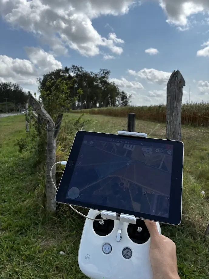 Tablet no controle do drone com imagem de satélite e plano de voo, ao lado de uma cerca e de uma lavoura